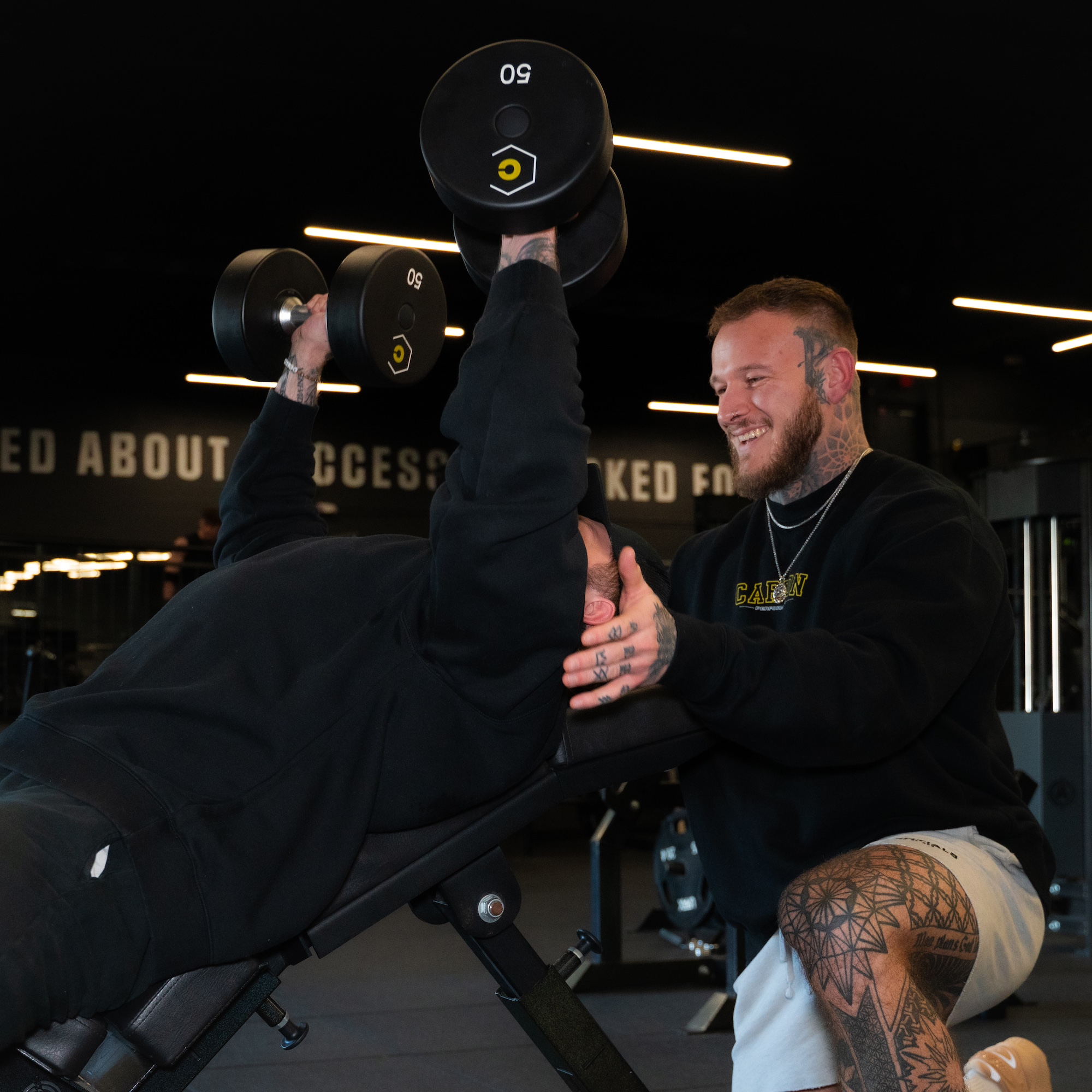 personal trainer at carbon performance gym in nashville tn spotting a gym member performing overhead press with dumbbells
