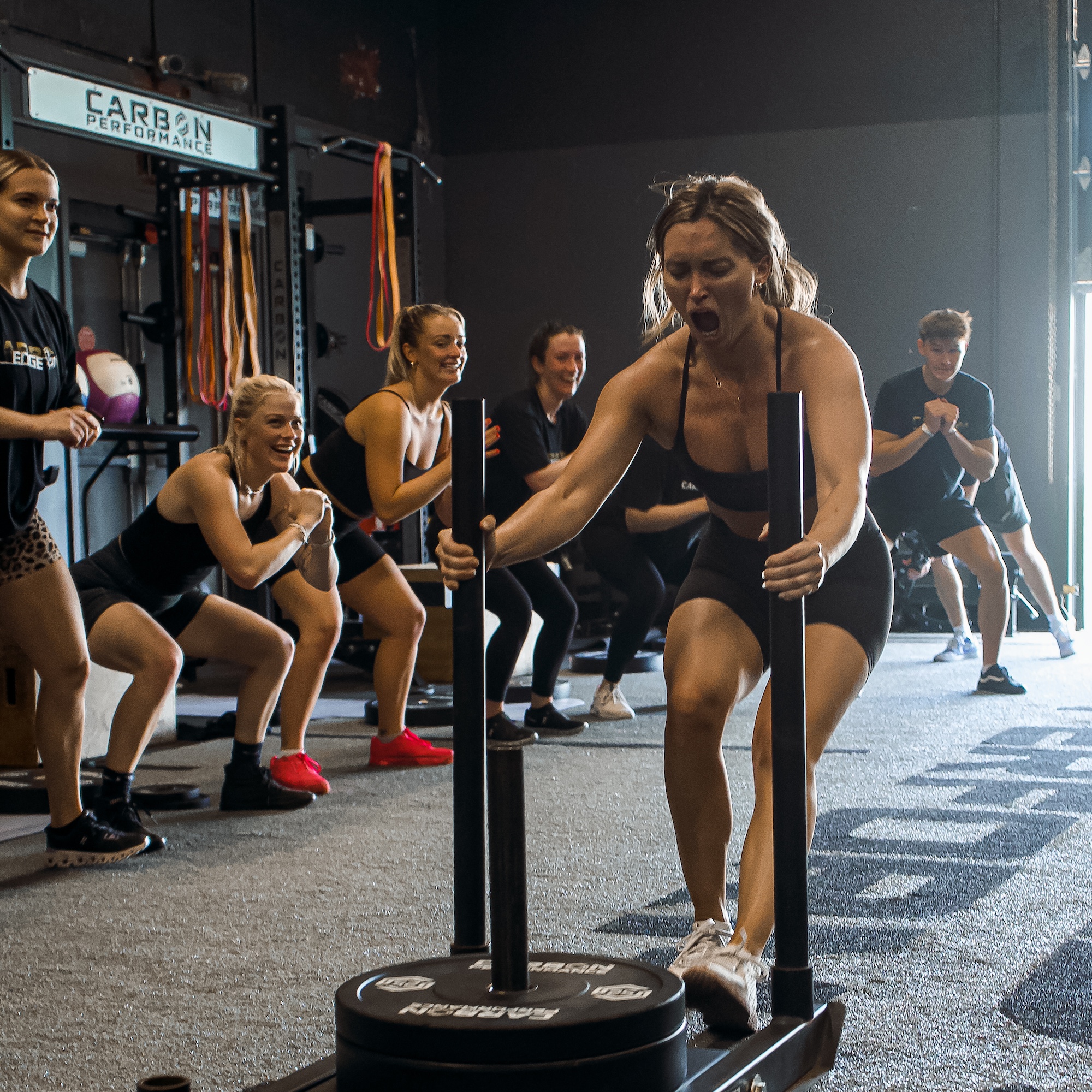 woman pulling weight training sled backwards during group fitness class at carbon performance gym in the nations in nashville tennessee