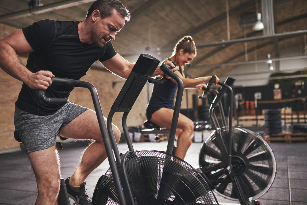 man and woman on assault bike to improve their fitness