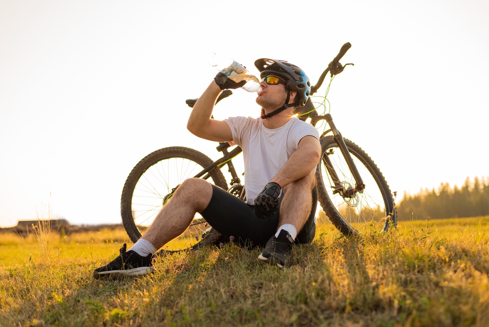 man outside sitting next to his bike drinking water after a long bike ride