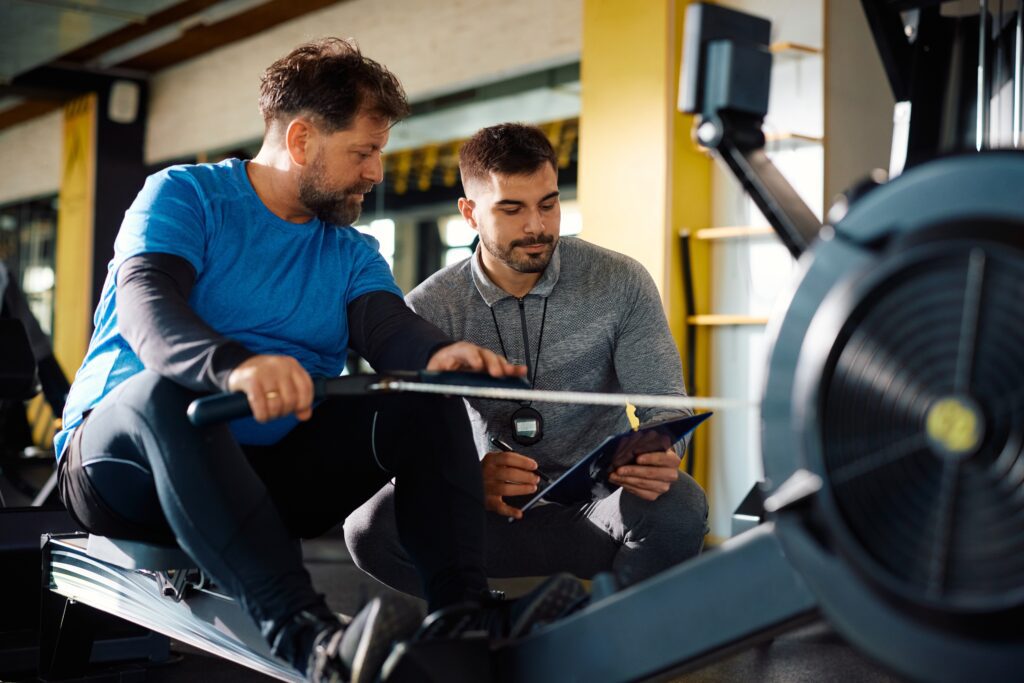 Personal trainer coaching gym goer on rower.