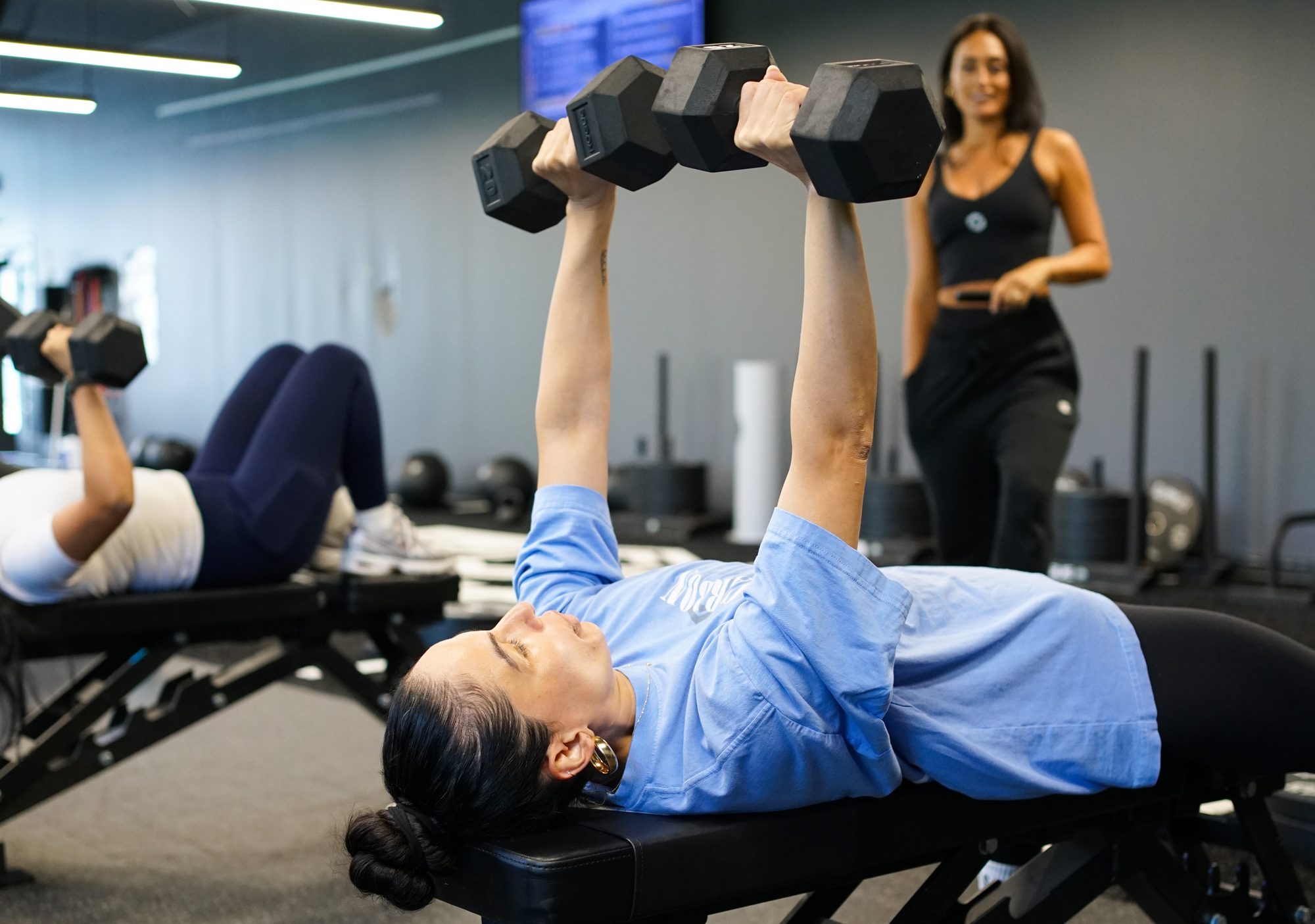 Woman doing a dumbbell chest press on a bench while a trainer watches at Carbon Performance
