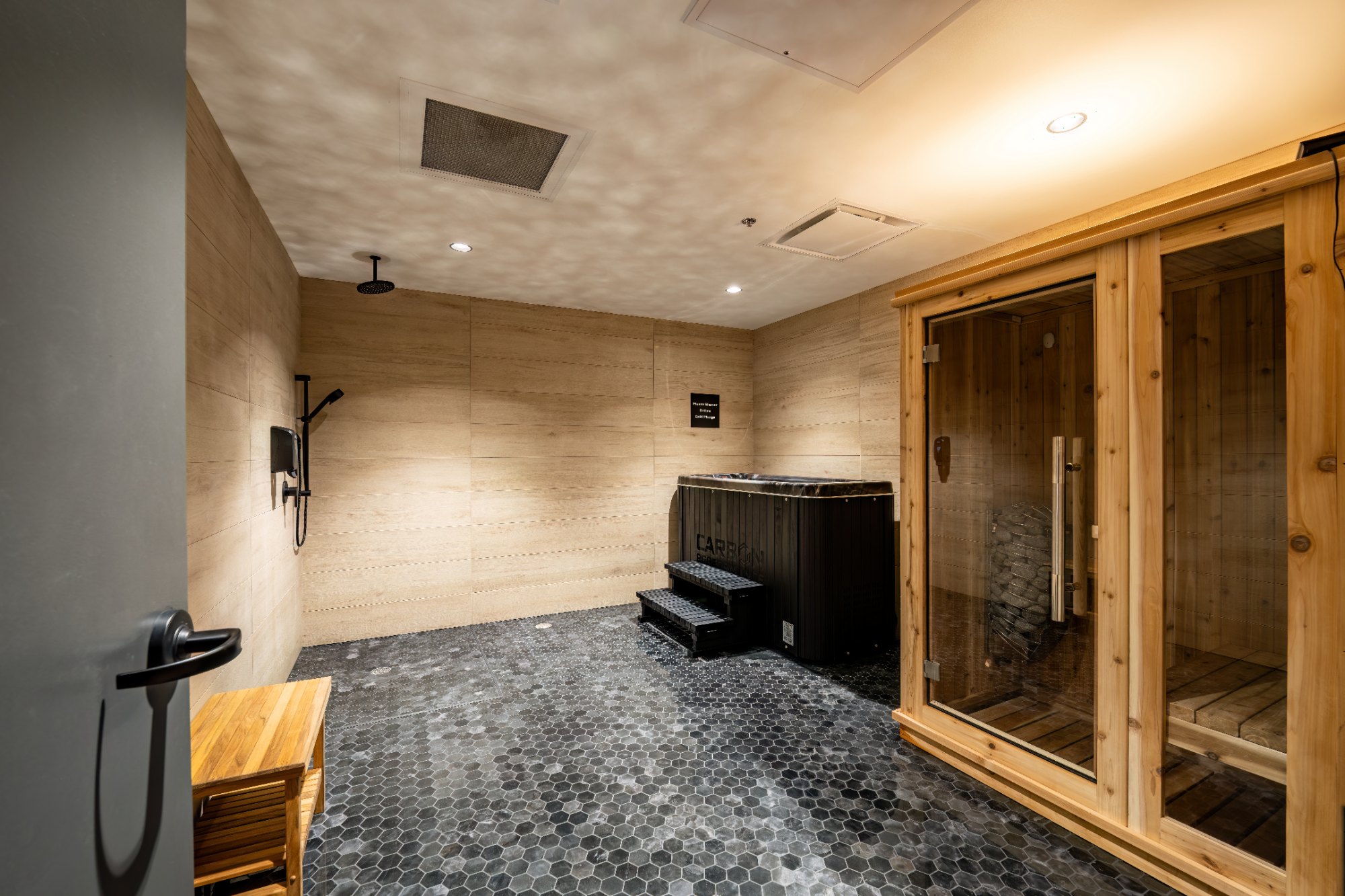Cold plunge tub, rinse shower, and cedar sauna in a stone-tiled recovery room