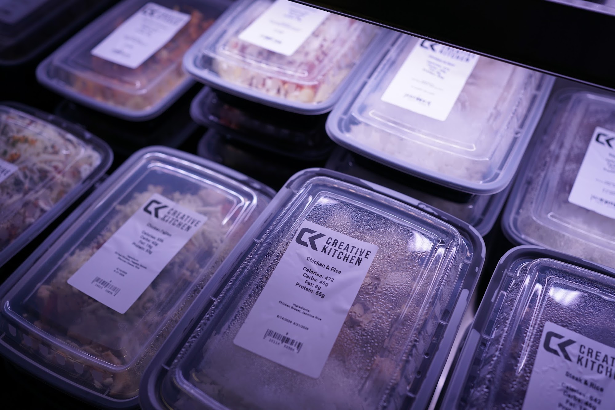 Labeled Creative Kitchen prepared meal containers stacked in a refrigerated display case